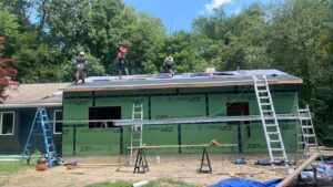 Construction workers on a roof during a home addition project, with green sheathing on the walls by Usa Construction of Danbury LLC in Danbury, CT.