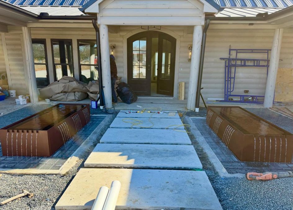 Home entrance under construction with dual water features and walkway by First Class Pools & Spas in Sachse, TX.