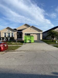 A green dumpster placed in a residential driveway for home junk removal by Bin There Dump That Dumpster Rental Orlando, FL.