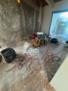 Room under home renovation with plastic sheeting, tools, and debris on an old wooden floor by International Wood Floors in Gaithersburg, MD