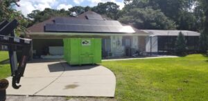A green dumpster placed in a residential driveway for home renovation junk removal by Bin There Dump That Dumpster Rental Orlando, FL.