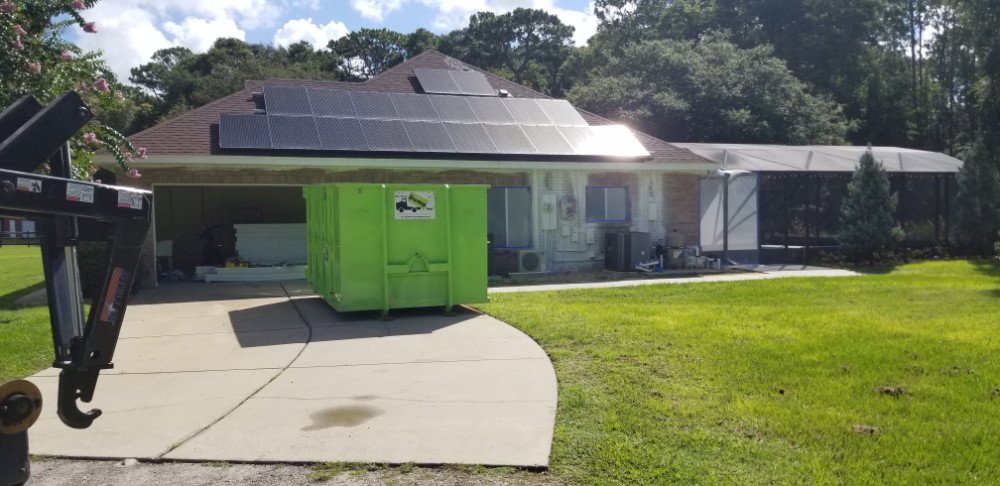 A green dumpster placed in a residential driveway for home renovation junk removal by Bin There Dump That Dumpster Rental Orlando, FL.