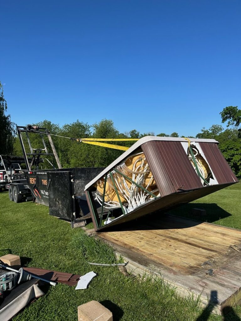 A hot tub being loaded onto a black dumpster/trailer for removal by All Seasons Junk Removal & Dumpster Services in Center Point, IA.