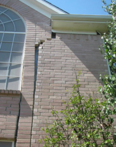 A severe vertical crack in a house's brick wall, indicating foundation repair work by Metro-Tex Foundation in Plano, TX