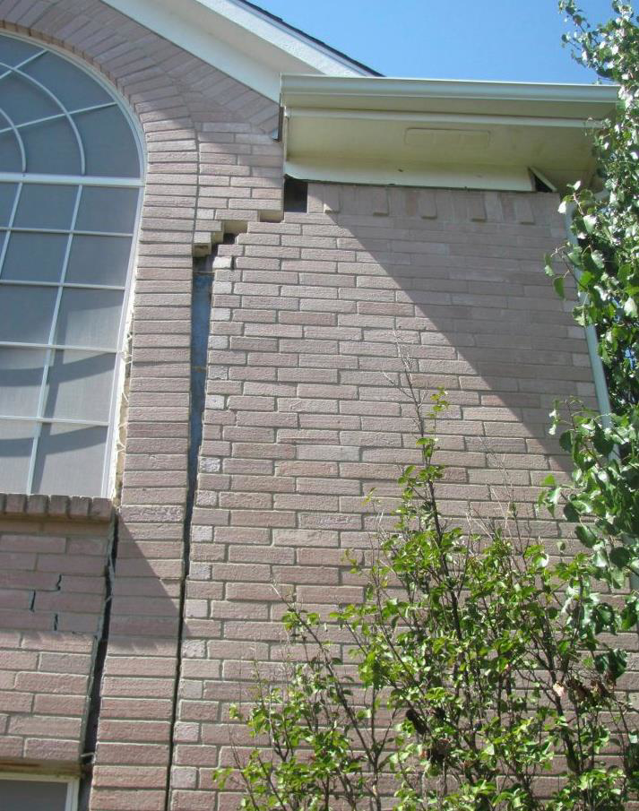 A severe vertical crack in a house's brick wall, indicating foundation repair work by Metro-Tex Foundation in Plano, TX