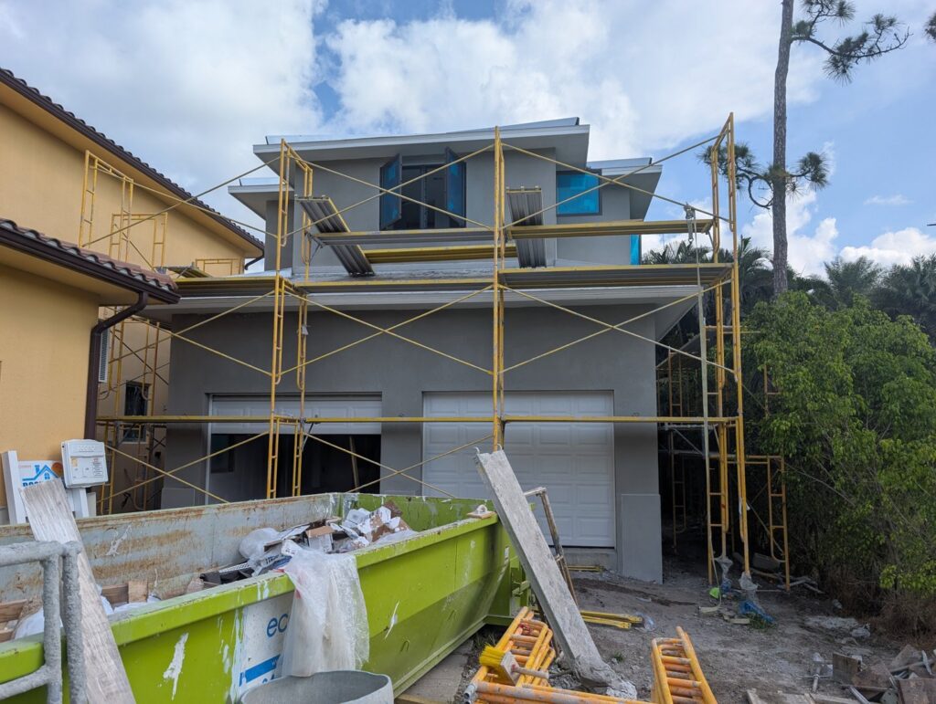 A house construction site with scaffolding and a dumpster, showcasing work by Rock's Custom Homes in St. Petersburg, FL.