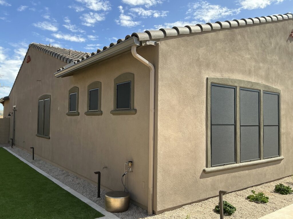 A house with dark sun screens installed on windows and a light-colored rain gutter, showcasing services by Phoenix Rain Gutters and Sun Protection in Glendale, AZ.