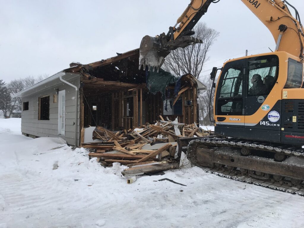 An excavator demolishing a house, generating debris for Expert Dumpster's junk removal service in Rochester, NY.