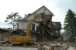 A wide shot of an excavator performing house demolition for All Gone Removal Demolition & Junk Dumpster Containers in Toms River, NJ.