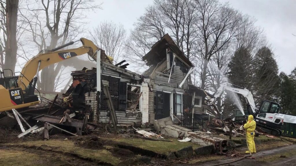 A house demolition site with two excavators and a worker, generating debris for Expert Dumpster's junk removal in Rochester, NY.