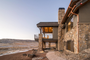 A house exterior featuring a wooden deck, stone chimney, and copper gutters by Lee Barker Builder LLC in Fort Collins, CO.