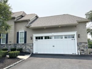 The exterior of a house showcasing a new white garage door, stone veneer, and stucco finish by RW Contracting Phila, LLC in Philadelphia, PA.