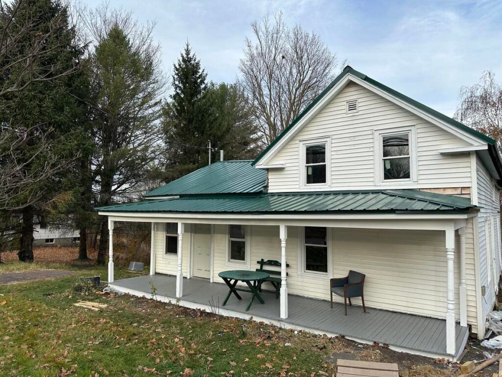 White house with a newly installed green metal roof and a renovated front porch by NS Construction in Imperial, CA.