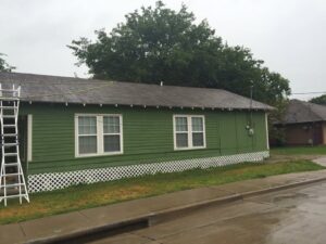 A green house exterior with a ladder leaning against it, indicating ongoing roof or exterior work by Texas Wounded Veterans Builders and Contractors in McKinney, TX.