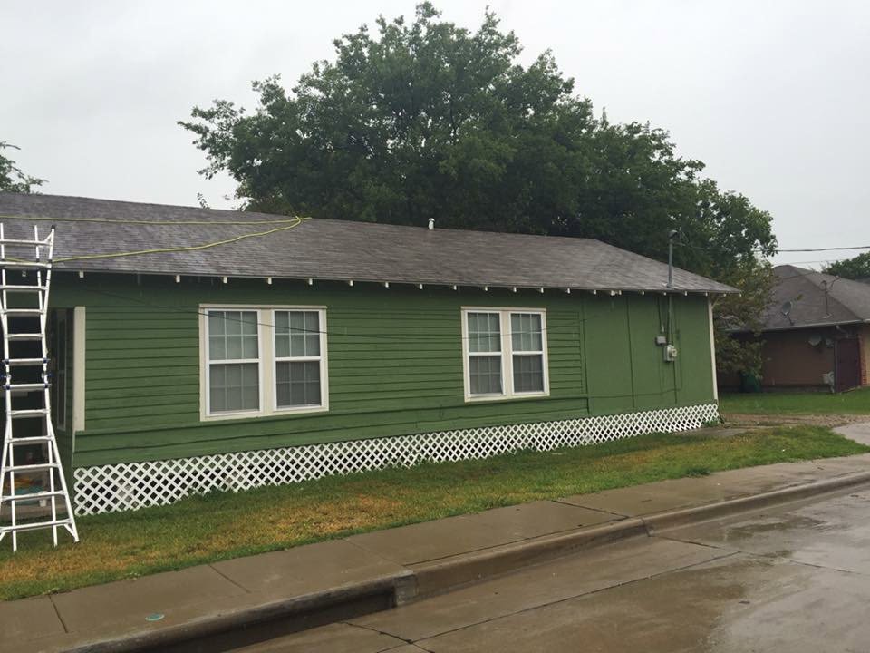 A green house exterior with a ladder leaning against it, indicating ongoing roof or exterior work by Texas Wounded Veterans Builders and Contractors in McKinney, TX.