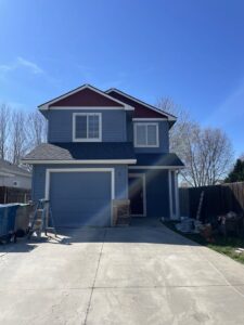 A newly painted blue house with red roof trim and a new garage door, showcasing exterior services by FES handyman services LLC in Boise, ID.