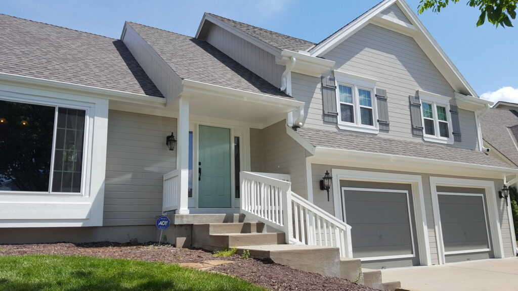 A house exterior with light gray siding, white trim, and a light blue front door, painted by E.L. Construction in Kansas City, MO.