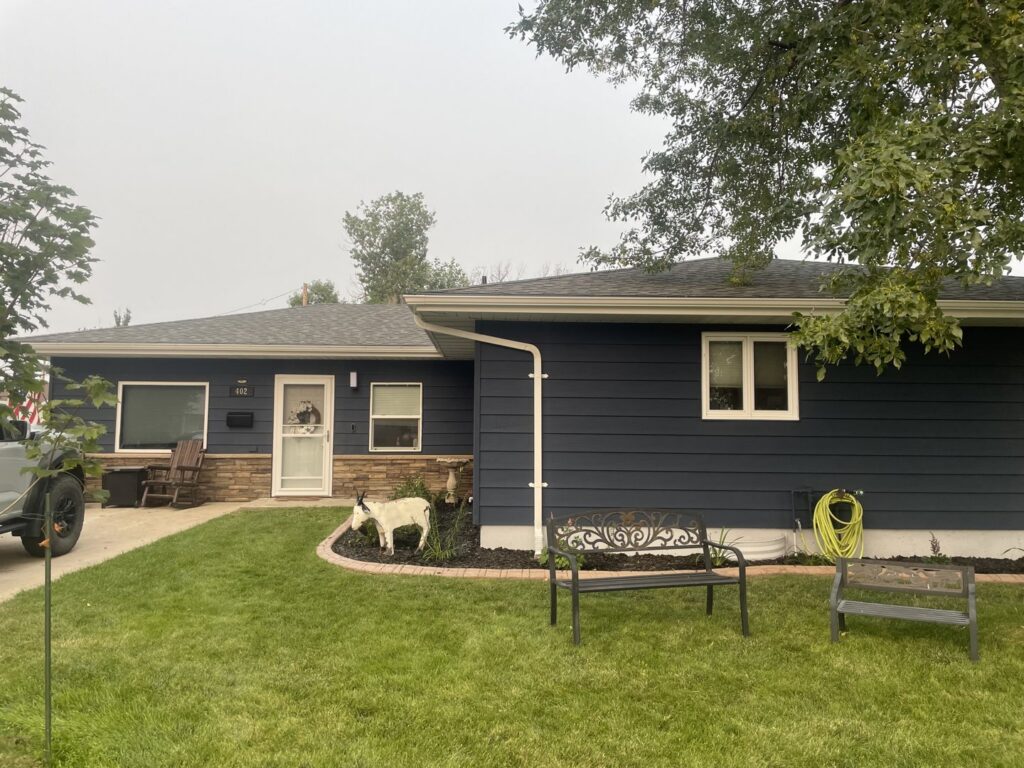 A beautifully renovated house exterior with dark blue siding, stone accents, and new landscaping by Knutson's Property Maintenance Llc in Williston, ND.