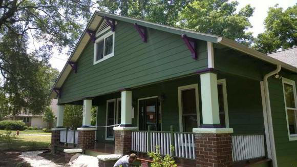 A residential house exterior undergoing renovation with green siding and brick columns by Randolph Residential Repair in Durham, NC.
