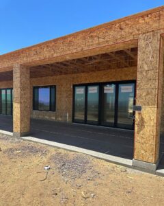 An exterior view of a house under construction with plywood sheathing and newly installed windows and doors by Kelso Custom Builders, Inc. in Phoenix, AZ.