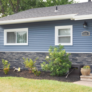 Exterior of a house with new blue siding and stone veneer installed by Patriot Construction in Rochester, NY