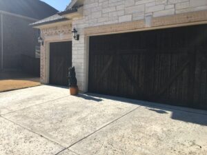 A house exterior featuring a stone facade, dark wooden garage doors, and a concrete driveway, completed by Texas Wounded Veterans Builders and Contractors in McKinney, TX.