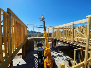 A telehandler lifting a wooden frame during house construction by Halo Development Inc. in Gilbert, AZ