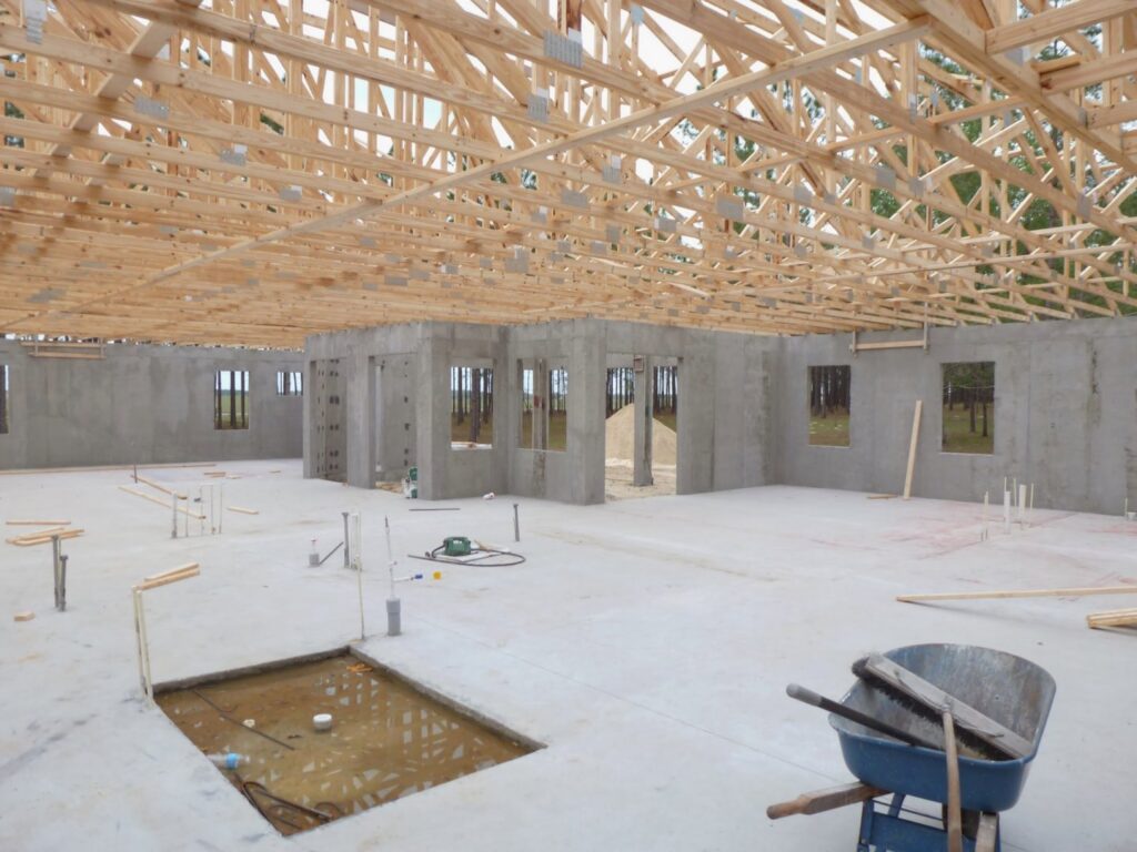 Interior view of a house under construction, showing concrete walls and wooden roof trusses by Cogdill Builders of Florida in Tampa, FL.