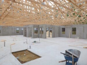 Interior view of a house under construction, showing concrete walls and wooden roof trusses by Cogdill Builders of Florida in Tampa, FL.