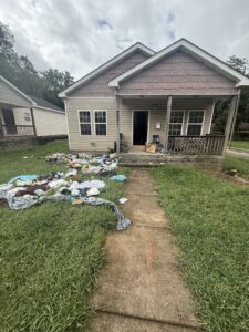 A house front yard with a large pile of clothes and other junk items scattered on the lawn for removal by LP Junk Removal in Birmingham, AL.