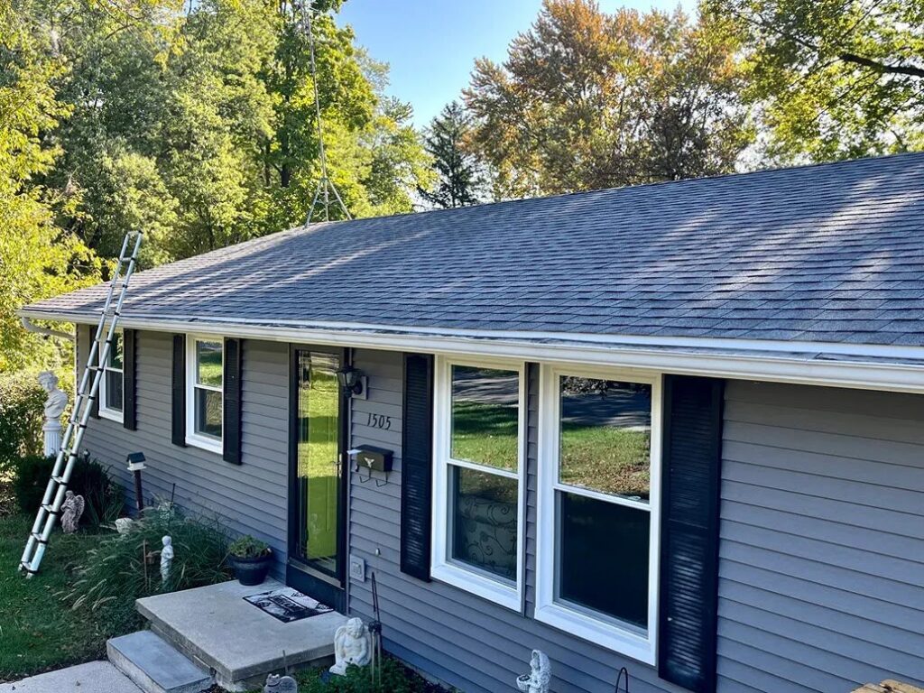The front of a house showcasing new gray siding, white windows, and a ladder, indicating ongoing work by Keep It Simple Construction LLC in Woodburn, IN.