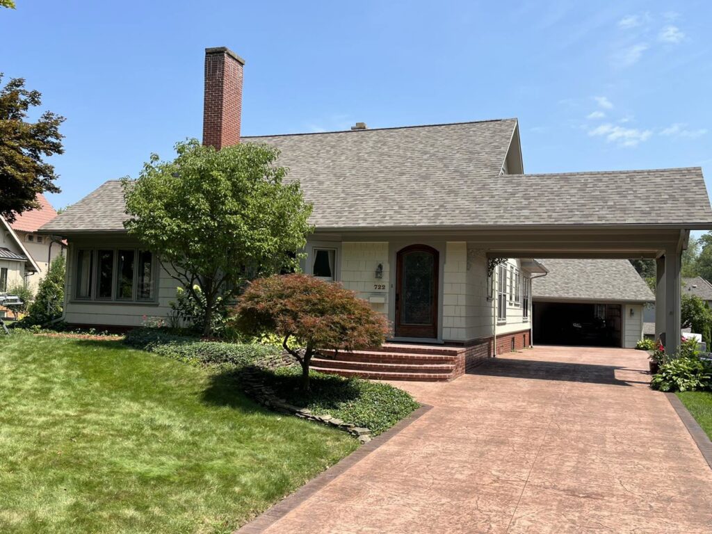 A house with a newly installed light brown shingle roof and an attached carport by Keep It Simple Construction LLC in Woodburn, IN.