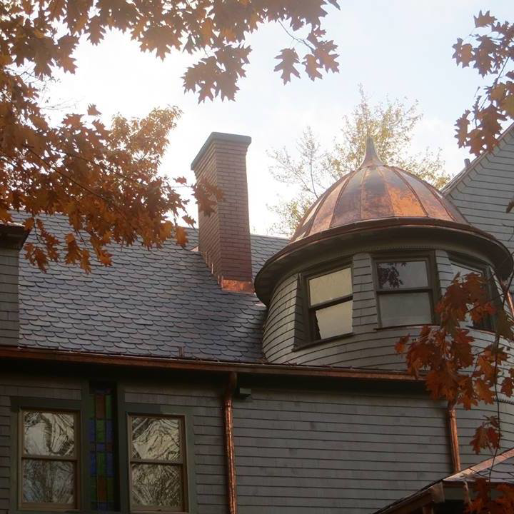 A detailed view of a house roof featuring a copper dome, slate shingles, and copper gutters by Copper & Slate Inc. in Buffalo, NY