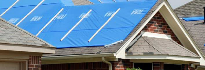 A house roof covered with a blue tarp after storm damage, handled by LEI Commercial Contractors in Houma, LA