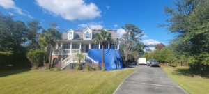 A house with a blue tarp on the roof and equipment in the driveway by WITTE CONSTRUCTION LLC in Mount Pleasant, SC.