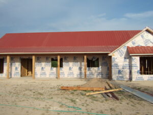 A house under construction with a red metal roof and walls wrapped in building paper by Austin Roofing and Construction in Austin, TX.