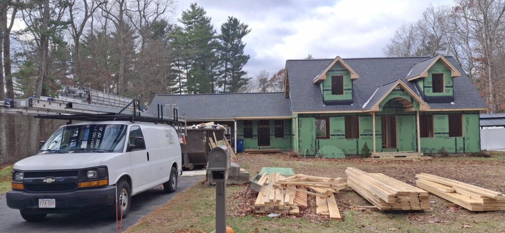 A house under construction with green Tyvek wrap and new roofing, showing a handyman job by Pinguil Roofing Siding Contractor in Lowell, MA.