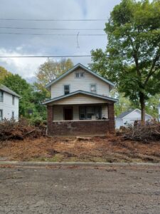 A house with a large pile of tree debris and a visible tree stump, indicating a recent tree removal service by Zepeda,LLC tree and bush removal in Rockford, IL.