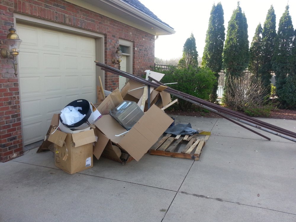A large pile of household junk, cardboard boxes, and construction debris on a driveway, ready for removal by All-Pro HAUL Property Services in Phoenix, AZ.