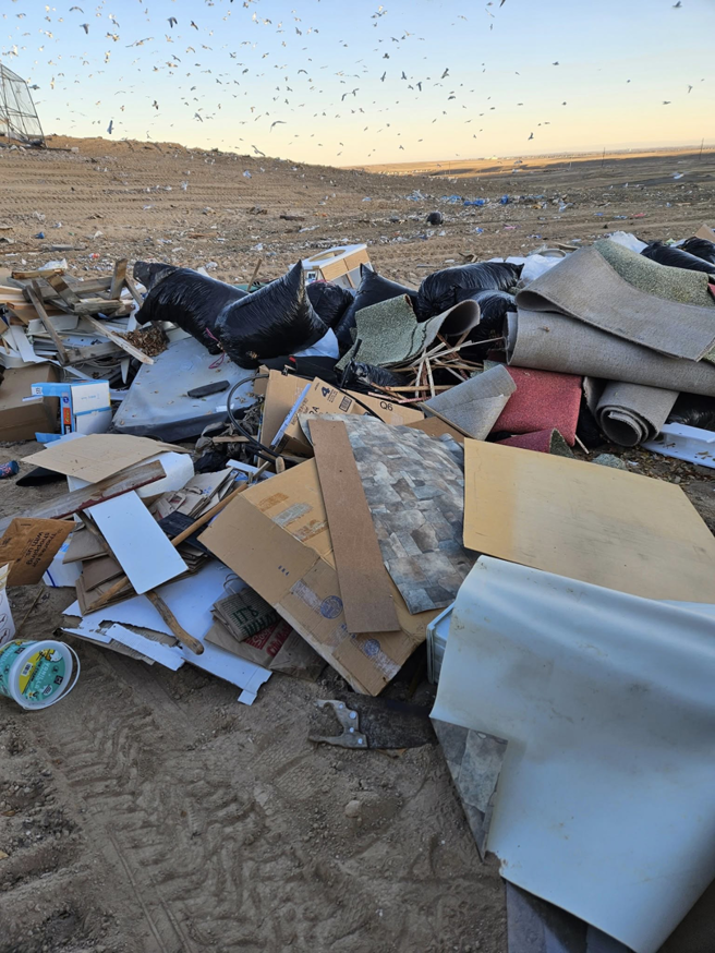 Household junk and debris, including boxes and miscellaneous items, piled on a driveway for pickup by We R Trash Inc. in Loveland, CO