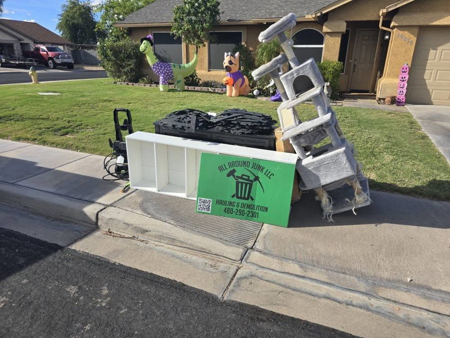 Household junk, including a cat tree and shelving, placed curbside with an ALL around junk, LCC sign for pickup in Mesa, AZ.