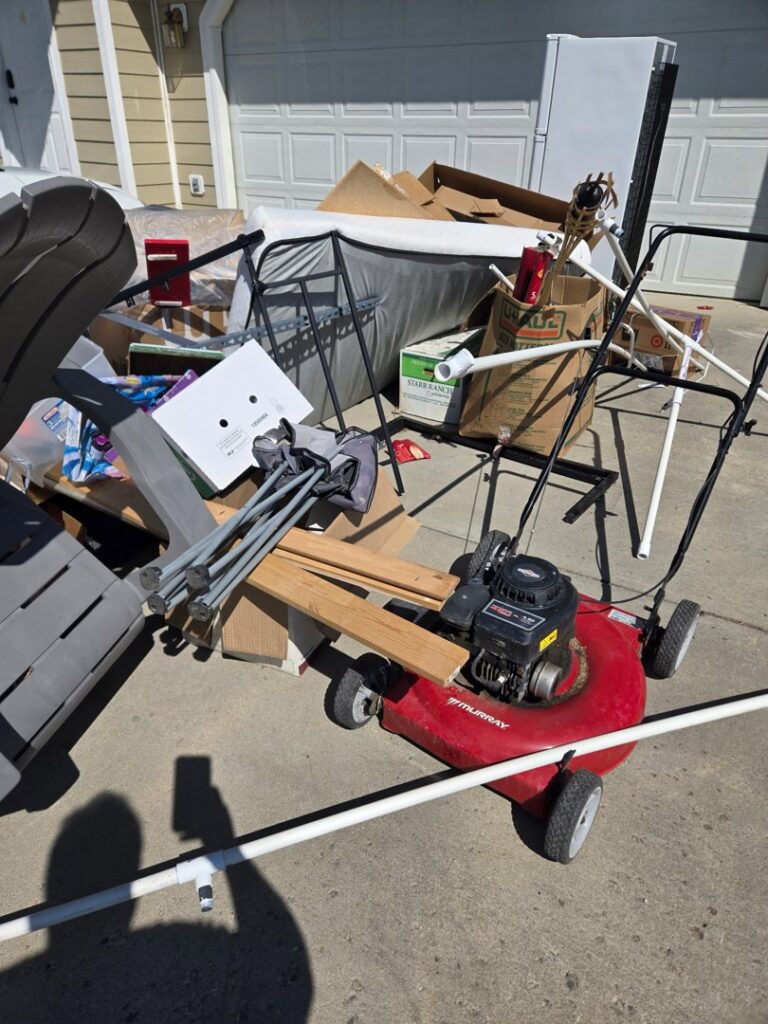 A large pile of household junk including a lawnmower, chairs, and boxes in a driveway, awaiting removal by Big Sky Junk Removal LLC in Billings, MT.