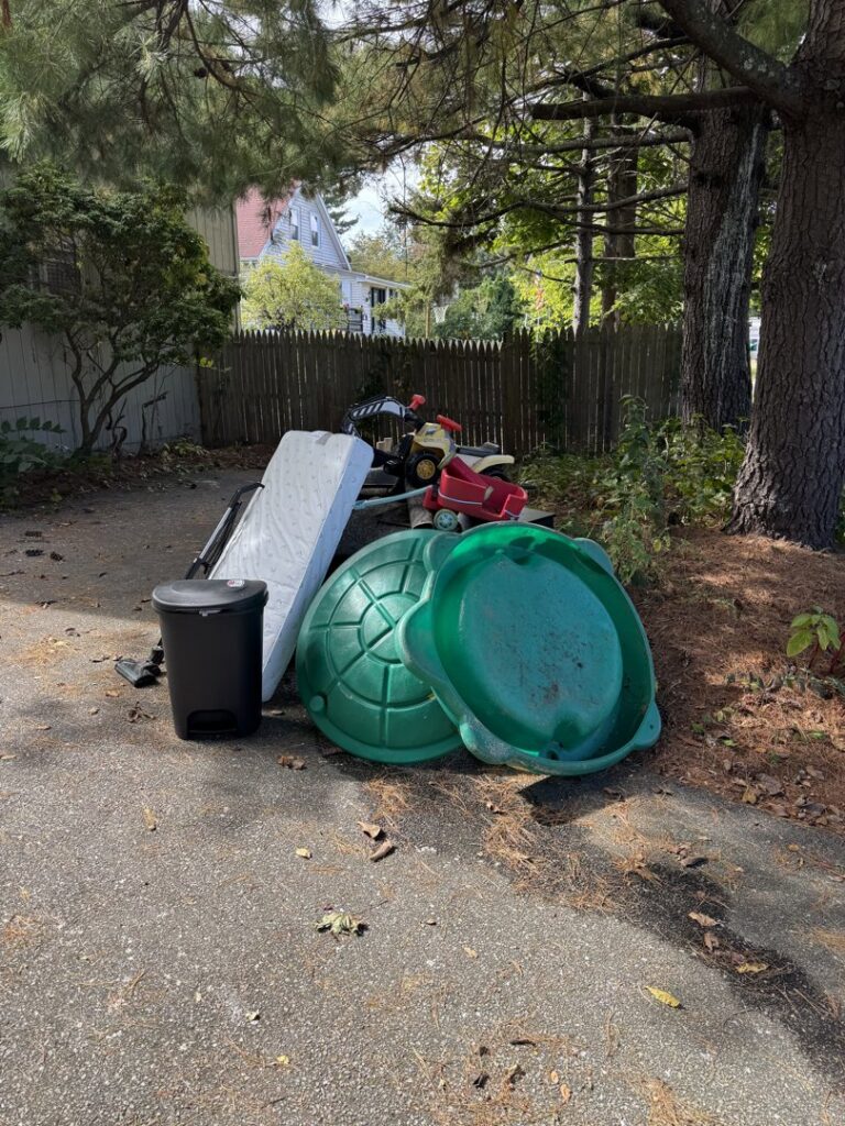 A pile of household junk including a mattress, sand turtle, and toys on a driveway, ready for removal by Junk Removal Brothers in Worcester, MA.