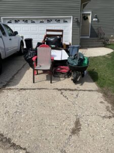 A pile of household junk including chairs, bags, and a wheelbarrow on a driveway, ready for removal by Anywhere Dumpster Rental in Naperville, IL.