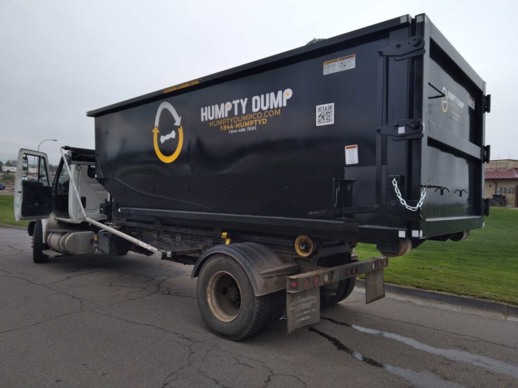 A Humpty Dump Roll-Offs & Dumpsters truck with a roll-off dumpster attached, parked on a street in Commerce City, CO.