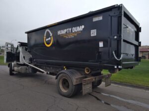 A Humpty Dump Roll-Offs & Dumpsters truck with a roll-off dumpster attached, parked on a street in Commerce City, CO.