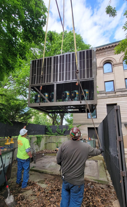 Workers from Jason Mechanical Corp installing a large HVAC unit with a crane outdoors in Joliet, IL.