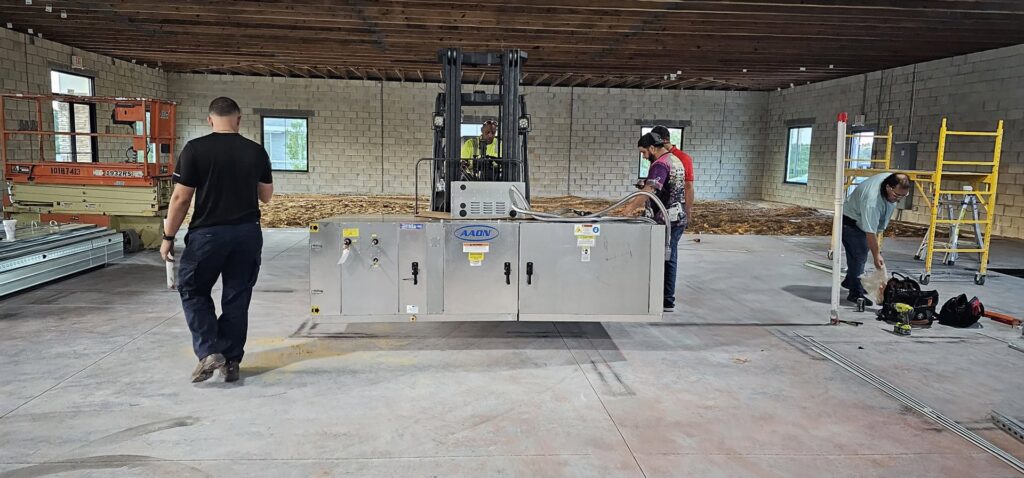 Construction workers using a forklift to place a large HVAC unit inside a building by Belair Inc. in Saint Cloud, FL