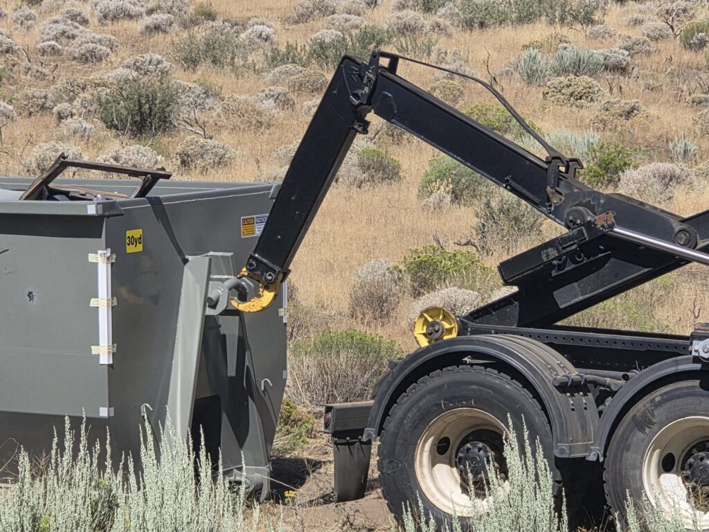 The hydraulic arm of a Trash Panda roll-off truck engaging with a dumpster in Carson City, NV.