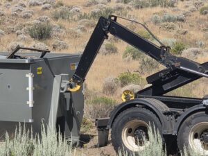 The hydraulic arm of a Trash Panda roll-off truck engaging with a dumpster in Carson City, NV.
